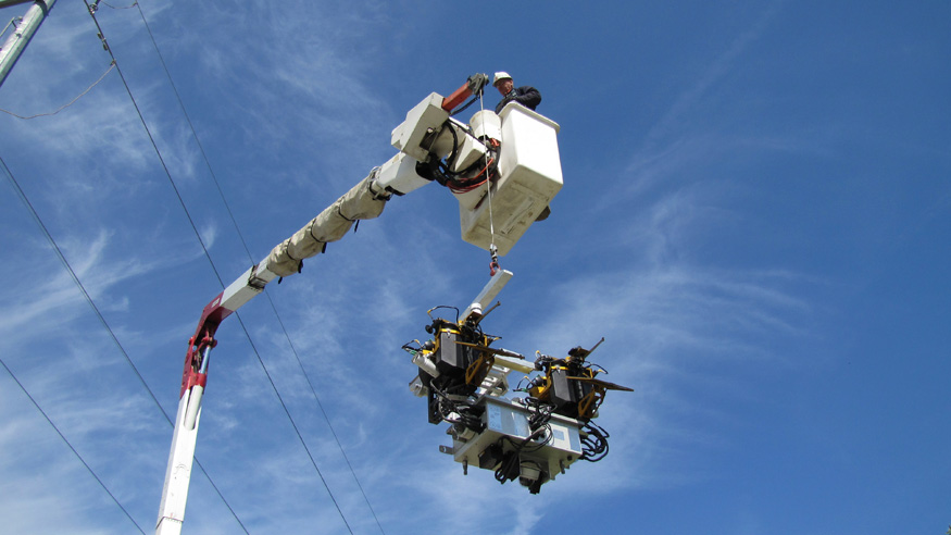 A technician uses a bucket truck as he prepares to attach Ti to a transmission line. The robot’s diagnostic equipment includes  high-definition cameras, LIDAR sensors, electromagnetic interference detectors along with data processing, global positioning, and communications systems.
